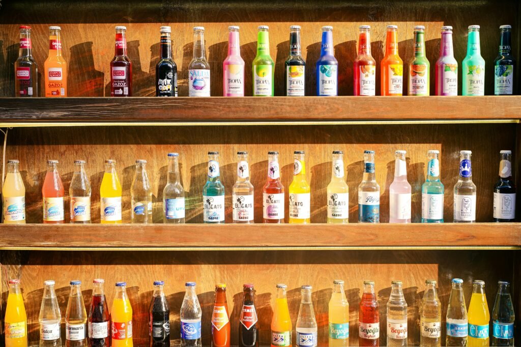 Vibrant display of various glass bottled drinks on wooden shelves under sunlight.